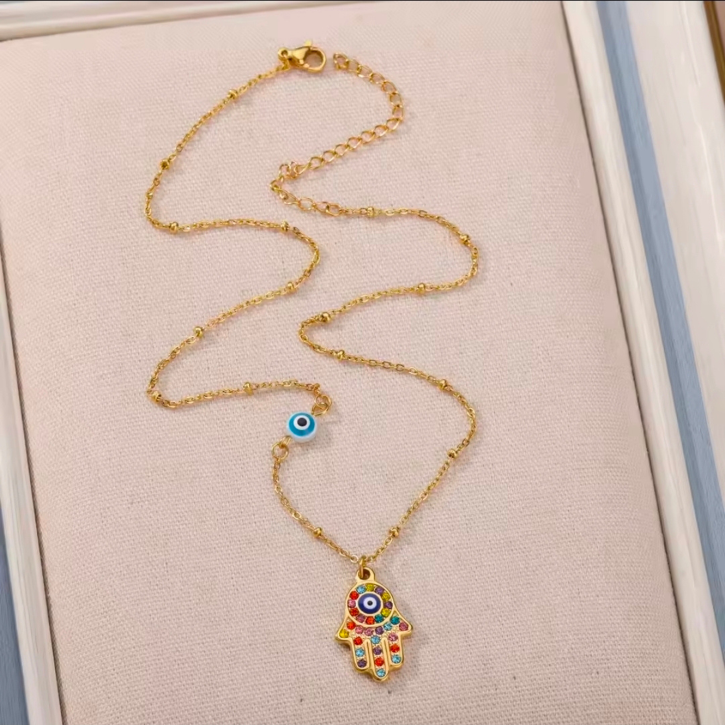 Gold necklace with a colorful evil eye pendant on a beige background