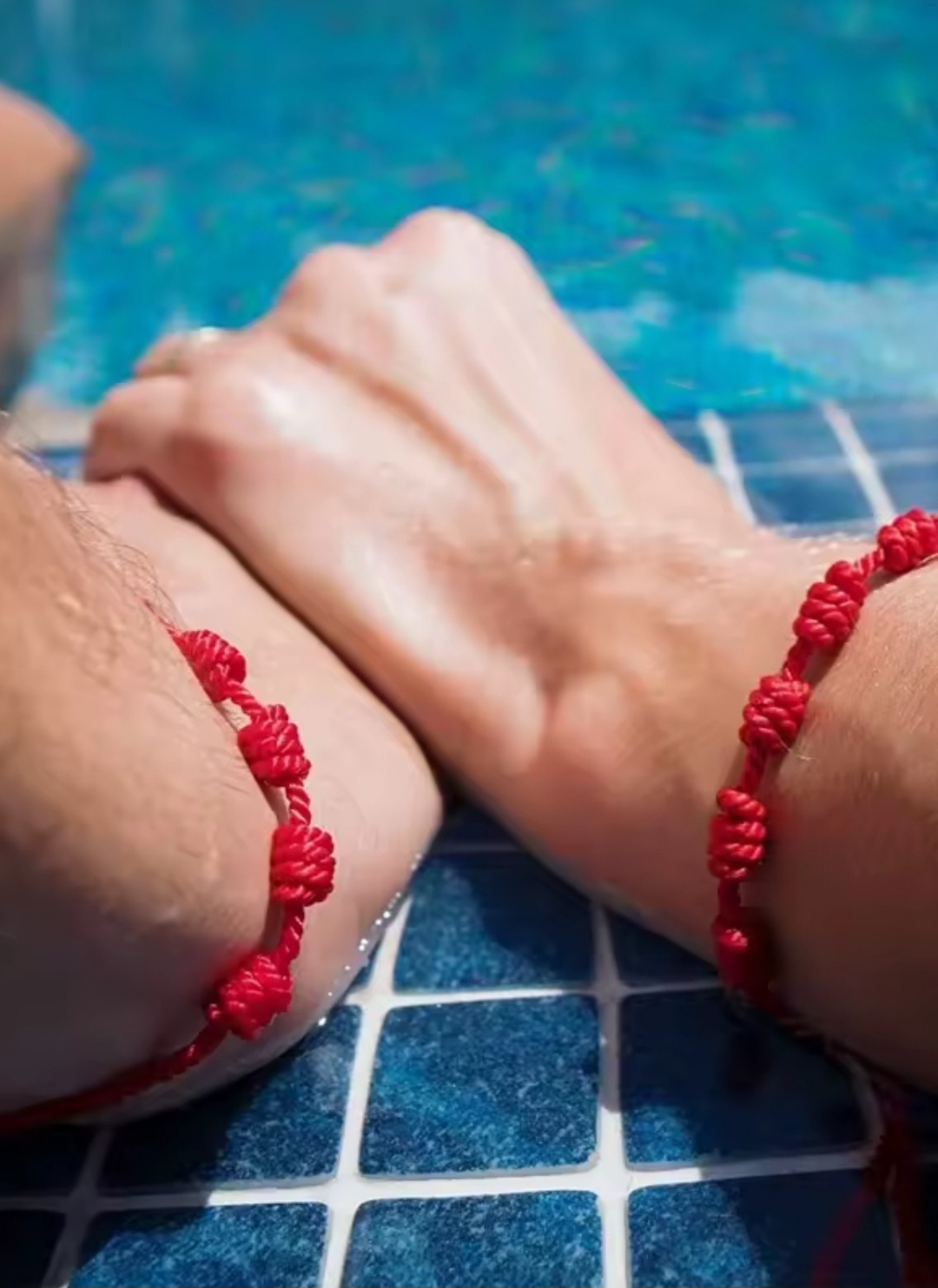 Close-up of arms with red bracelet on a blue tiled floor.