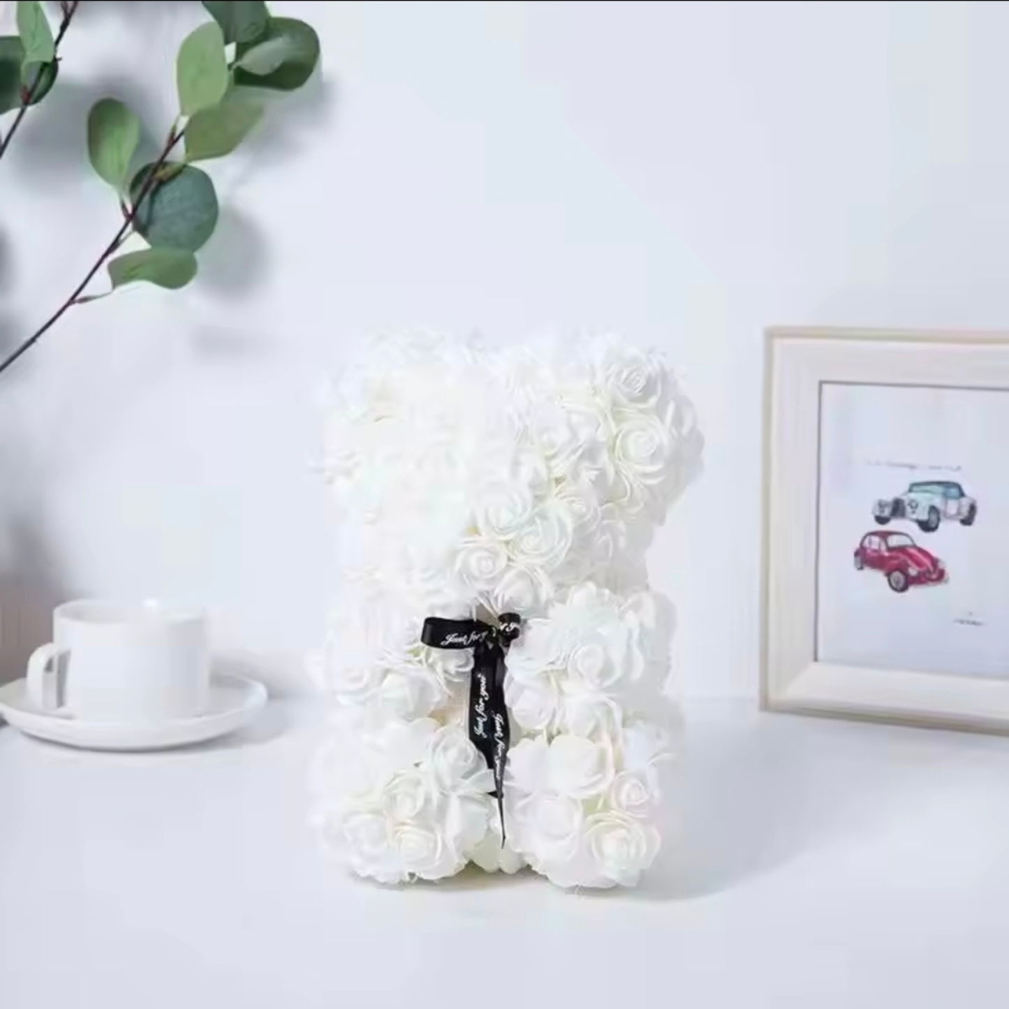 White floral arrangement on a table with a cup and saucer and a framed picture in the background.