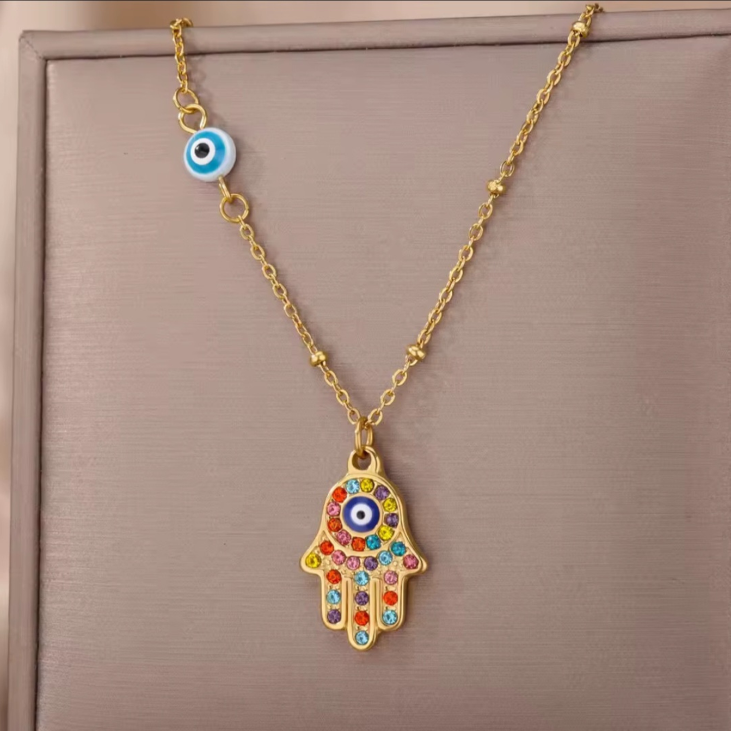 Necklace with a colorful Hamsa hand pendant and evil eye charm on a beige background