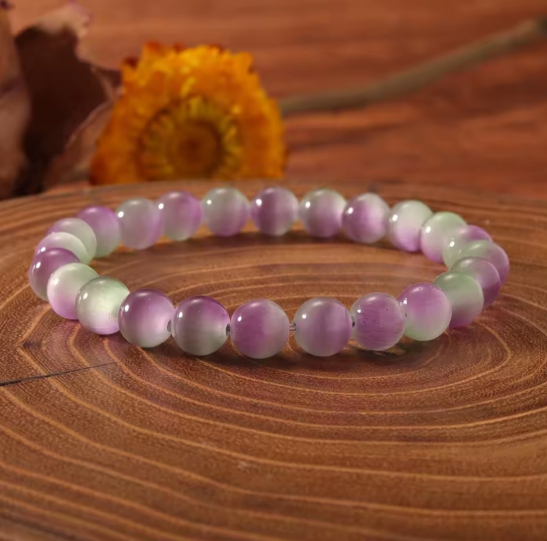 Beaded bracelet with purple and green beads on a wooden surface with a blurred flower in the background
