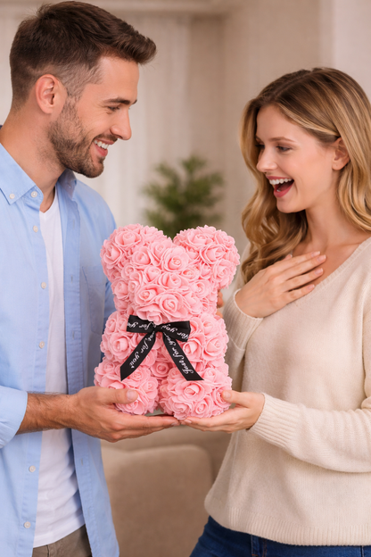 Man and woman holding a pink teddy bear made of roses with a black bow.
