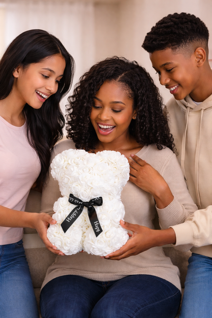 Three people holding a white teddy bear with a black ribbon and text.